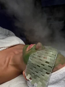 Client receiving a green facial mask with jade stones and steam at Parie Med Spa