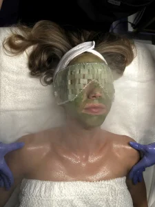Client receiving a green facial mask with jade stones and steam at Parie Med Spa