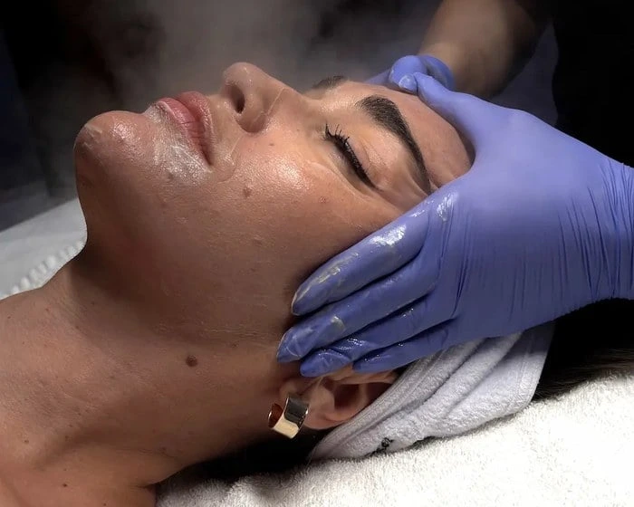 Gloved hands cleansing a model's face at the start of a facial